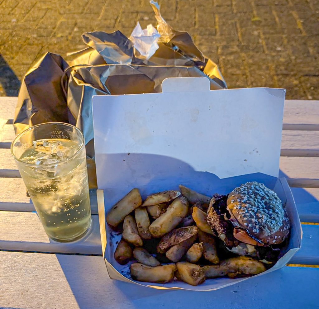 A gluten free burger and lime cordial drink sit on a bench outside a conference centre.